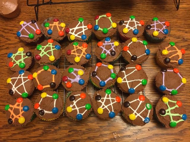 2 dozen cupcakes on a cooling rack. Each has a graph iced on with 5 M&M vertices, some are a pentagon and some are a 5 pointed star